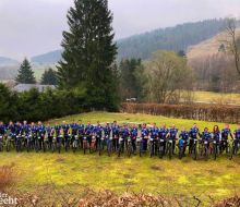 Viele Radfahrer stehen in einer Reihe auf einer Wiese, im Hintergrund Upländer Berge