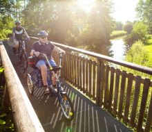 Radfahrer und ein Sesseldreiradfahrer auf der Bruecke über die Diemel bei Warburg