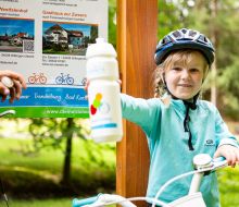 Ein Kind hält eine Trinkflasche vor der Infotafel in Willingen-Usseln hoch