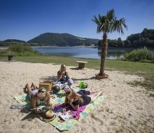 Muetter mit Kindern sitzen auf einer Decke im Sand und picknicken, im Hintergrund der Diemelsee